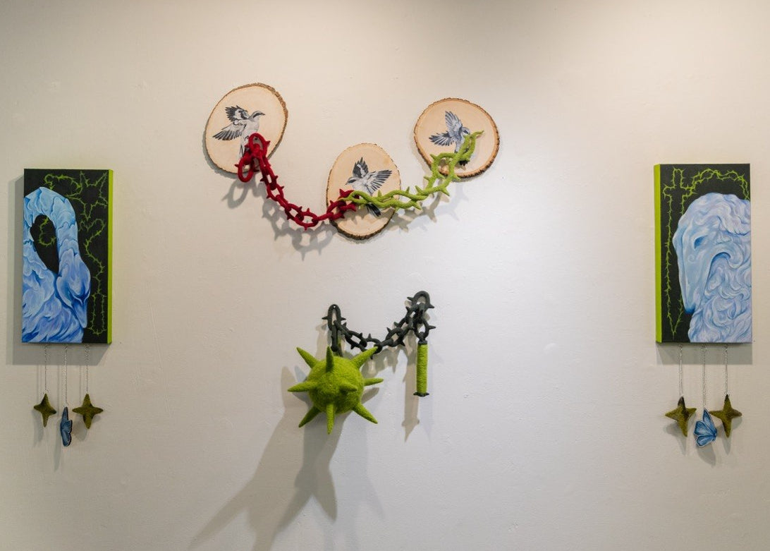 paintings with blue swan and blue dog on either side of a felted mace and three bird paintings on wood rounds